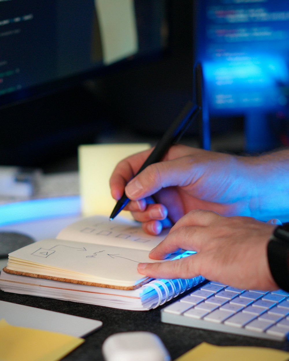 Hand macht Notizen vor einem Bildschirm mit Programmcode
